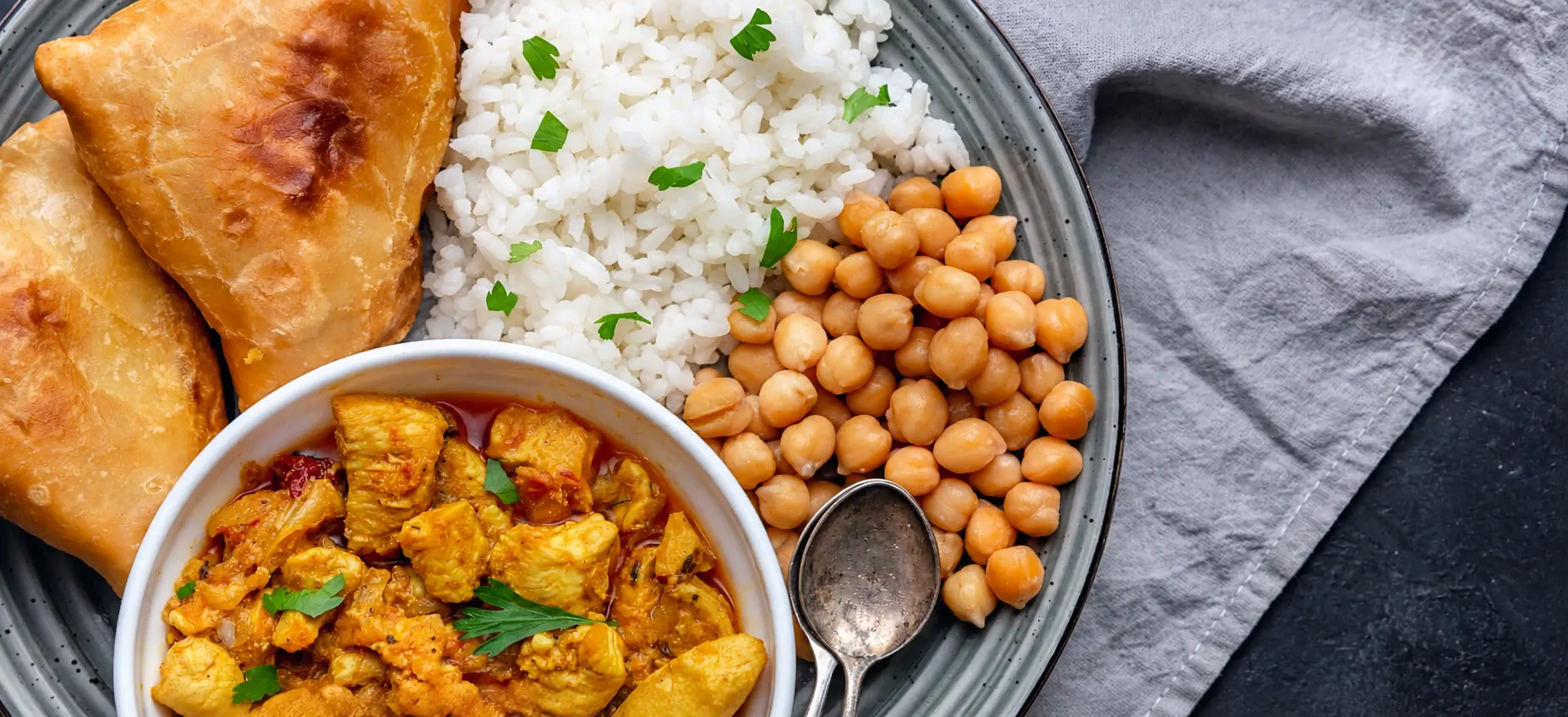 A plate of samosas, rice, chickpeas and chicken curry
